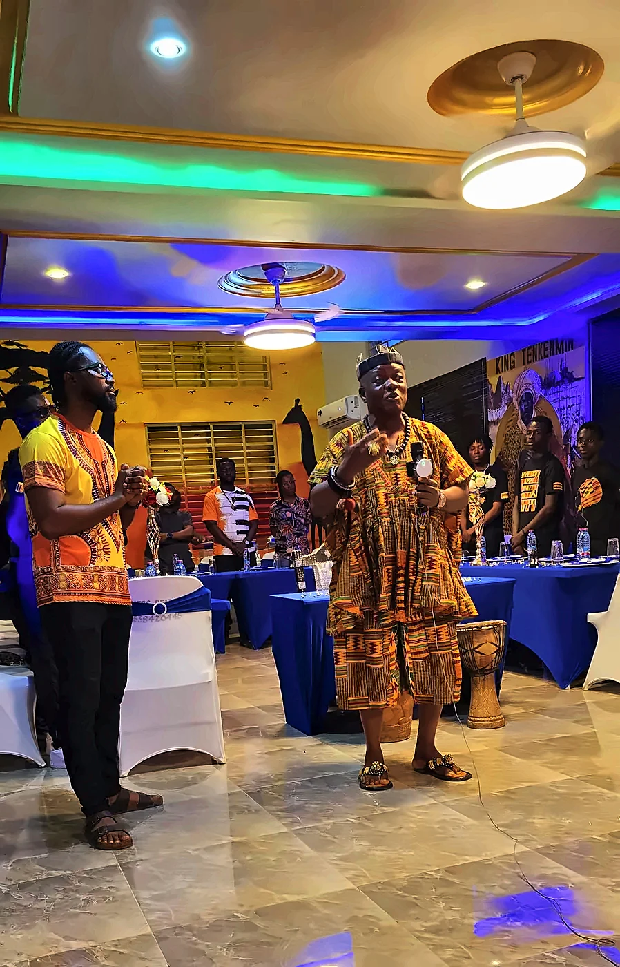 Presenters in traditional Ghanaian dress speaking in the event hall