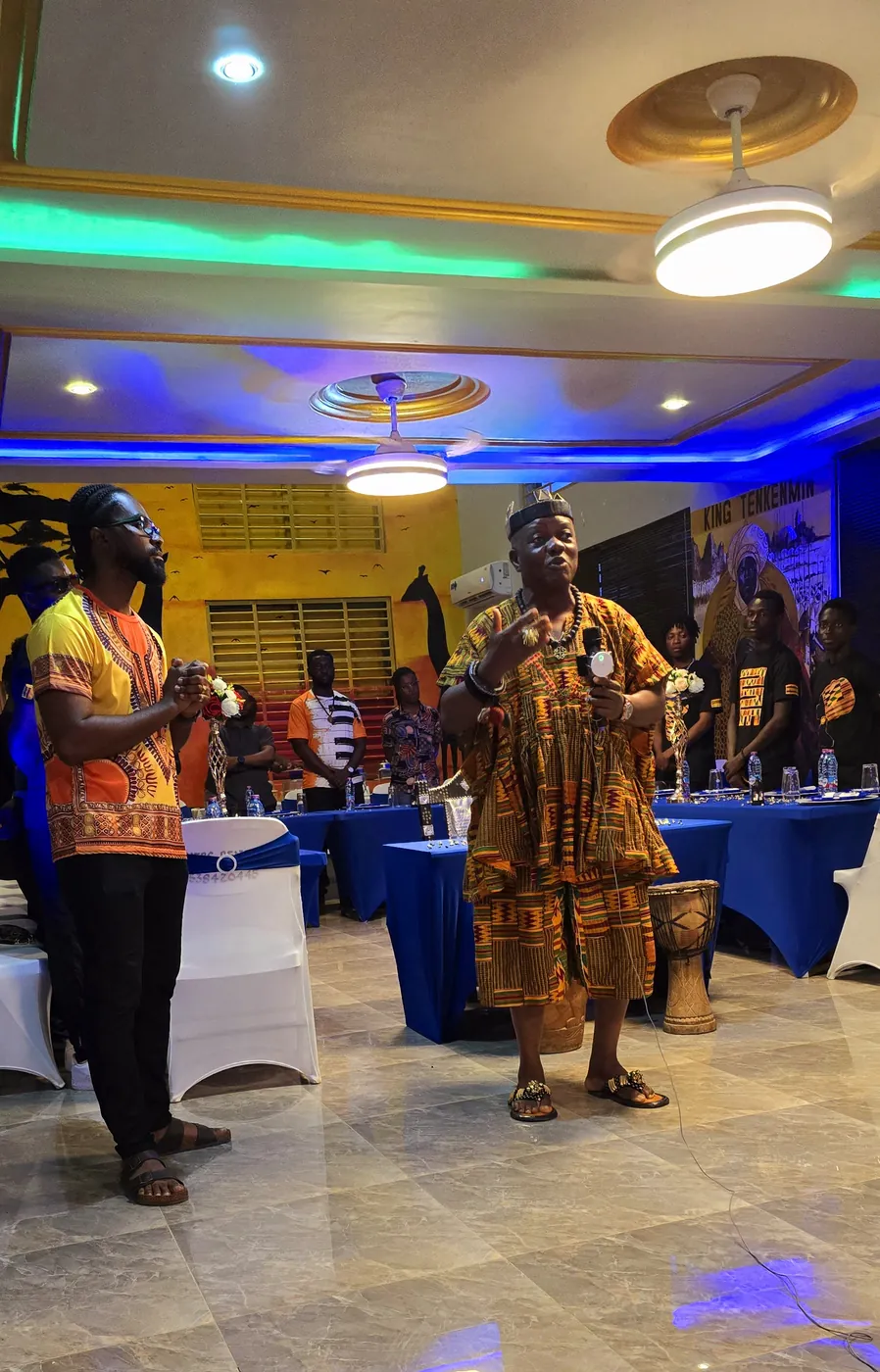 Presenters in traditional Ghanaian dress speaking in the event hall