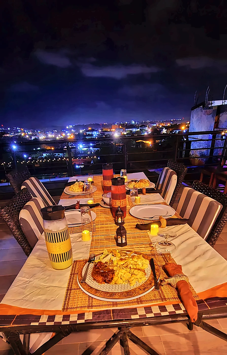 Candlelit dinner table set on the rooftop terrace at night, overlooking the lights of Cape Coast