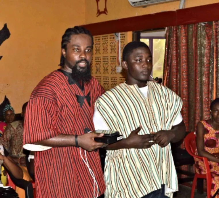 An Oiada presenter in traditional Ghanaian dress with a student